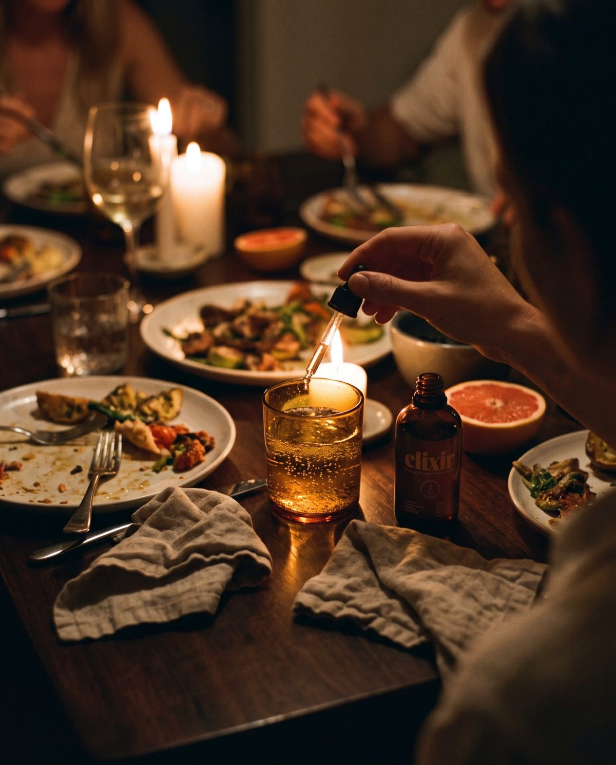 three pipettes of elixir into a glass of tonic at a candlelit dinner