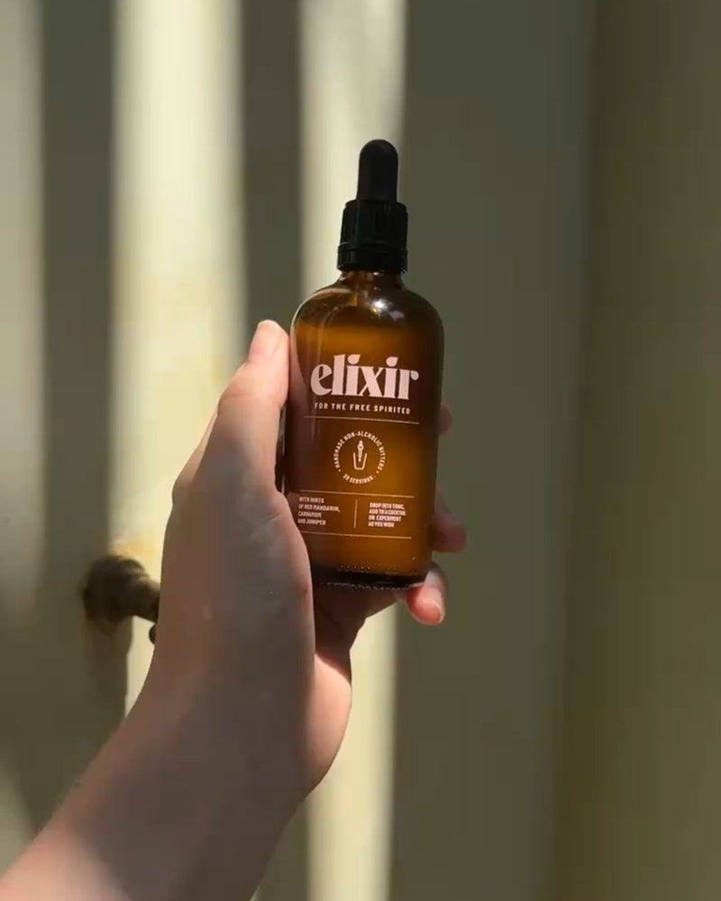 A hand holding an elixir bottle  against a window with light streaming through.