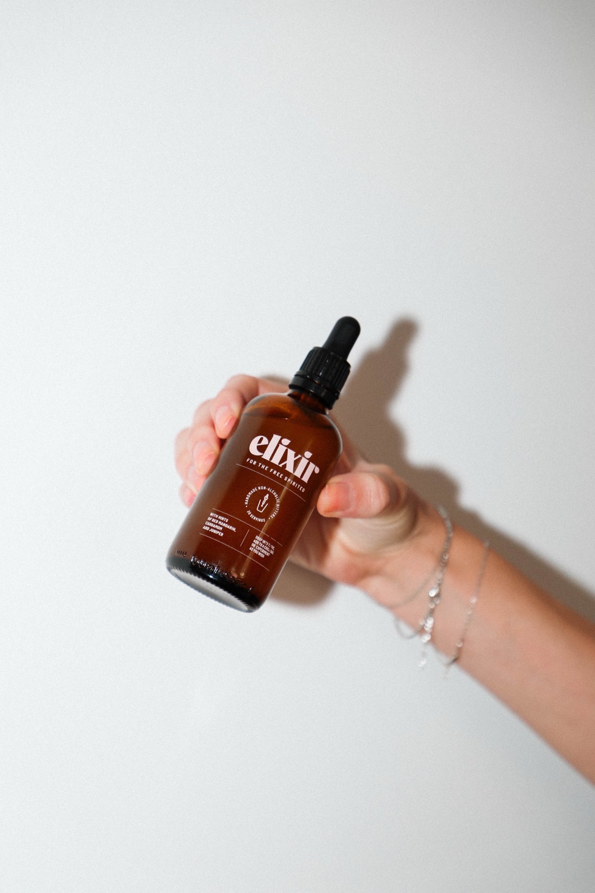 A hand holding the Elixir dropper bottle against a white wall