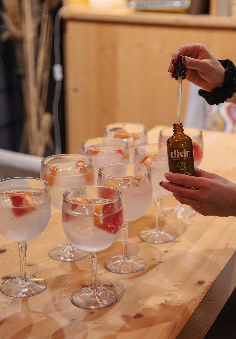 Person pouring elixir into a glass with fruit on a wooden table.