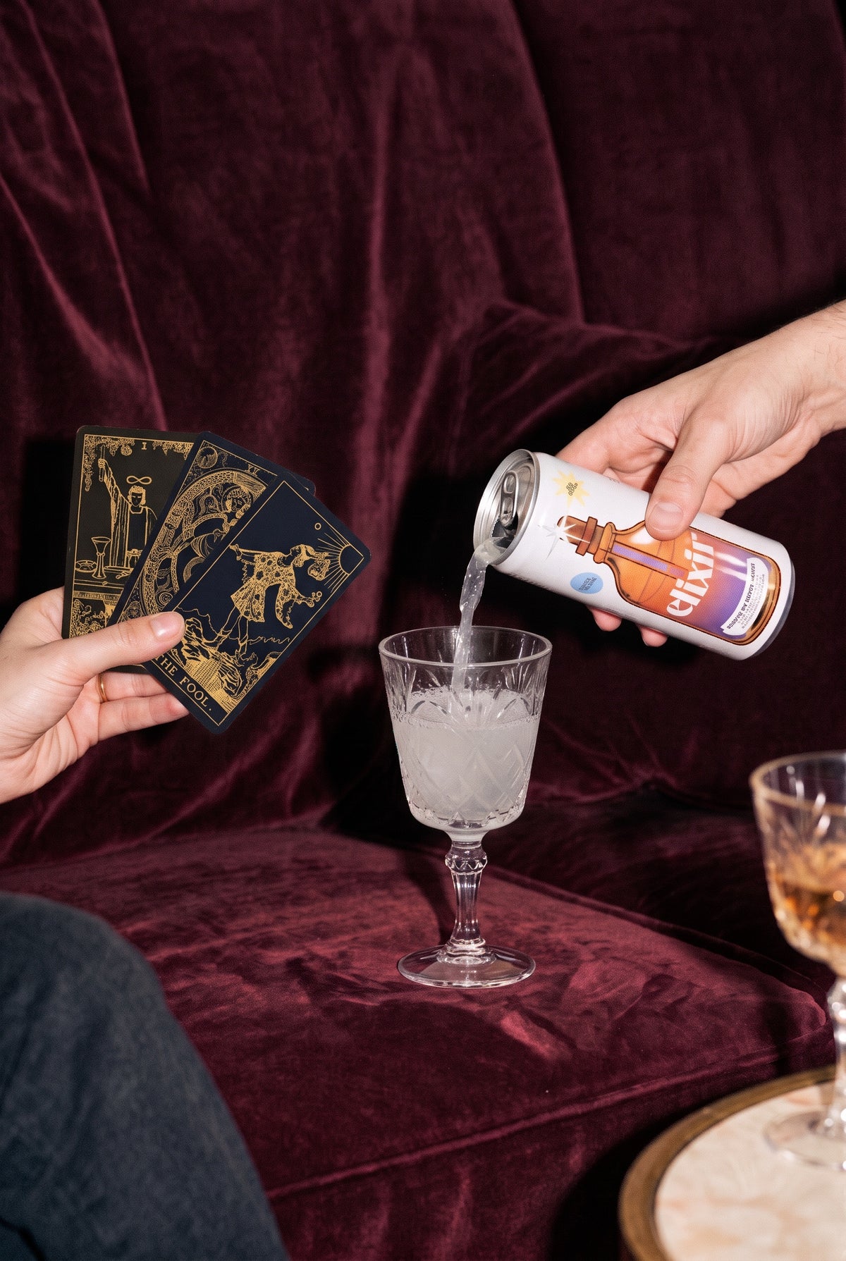 A can of E&T poured into a cut-glass goblet beside a hand of tarot cards on red velvet